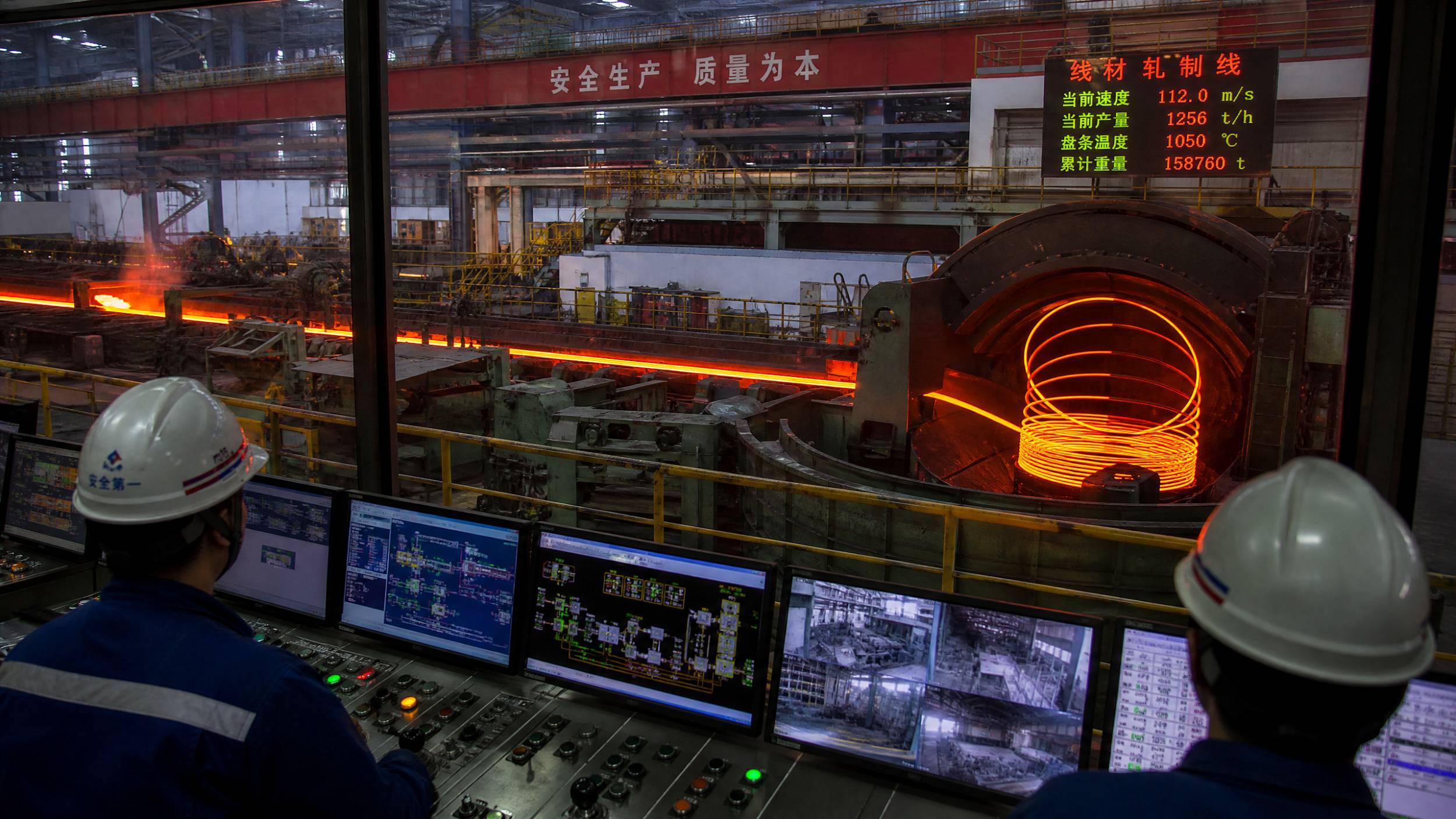The interior of a high-tech steel mill in China showing a red-hot steel wire rod being coiled at high speed with workers monitoring from a control room.