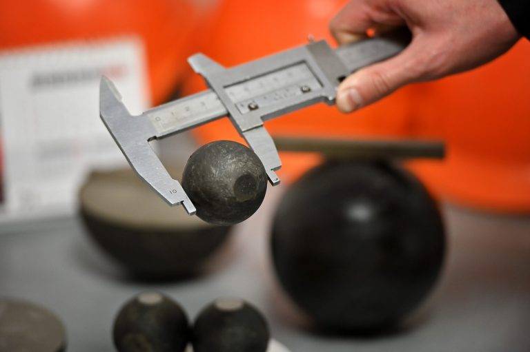 Technician measuring grinding ball diameter with digital caliper during quality inspection