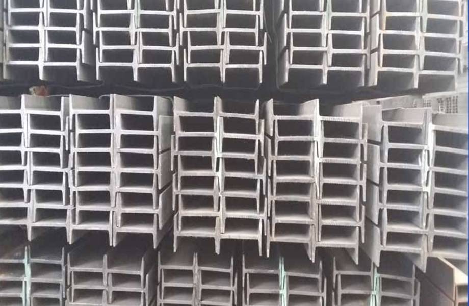 A large stack of heavy I-beam steel sections in a bright, modern industrial warehouse.