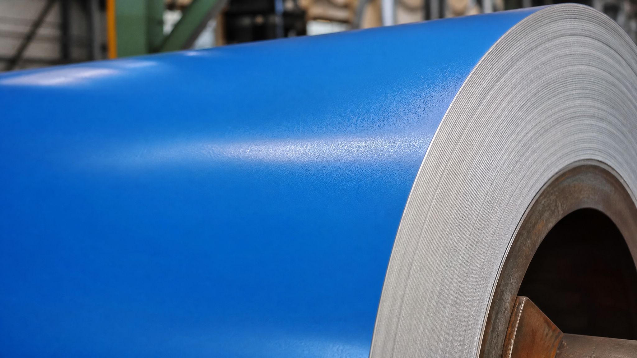 A sharp, close-up photo of the edge of a blue PPGI steel coil, showing the smooth, vibrant color coating and the metallic layers.