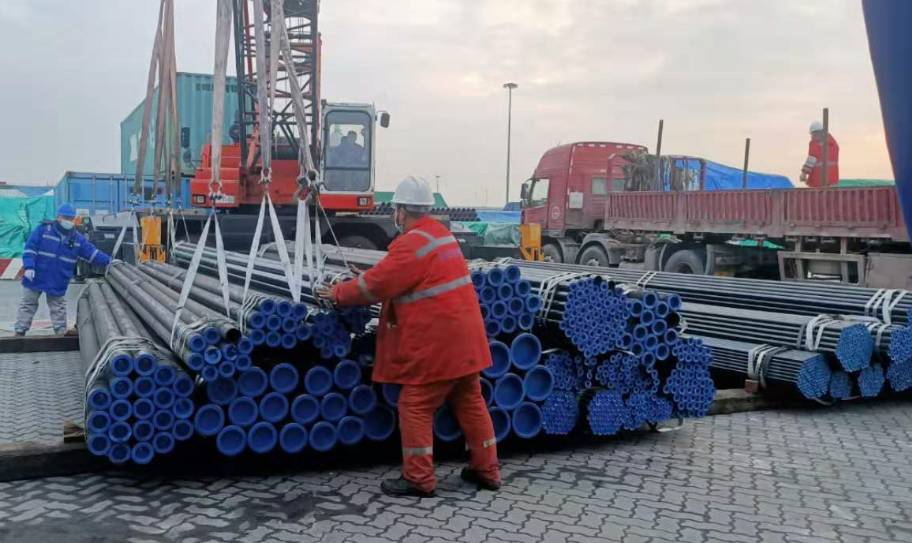 Workers loading bundles of steel pipes with crane at shipping port