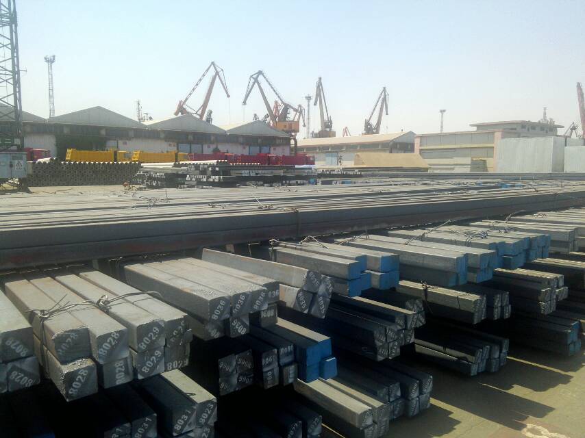  Bundles of steel billets being loaded onto a large cargo ship at a busy port.