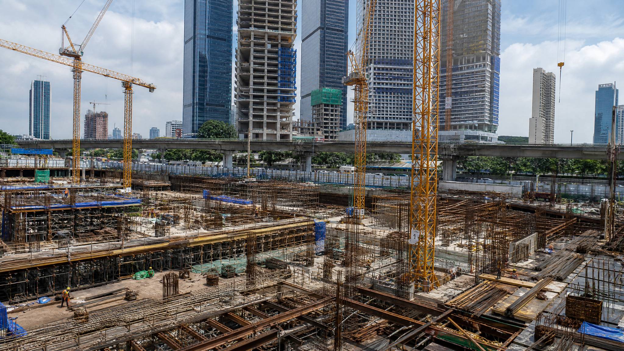 A large construction site in Jakarta with cranes and numerous structural steel beams and rebar in use for high-rise buildings.