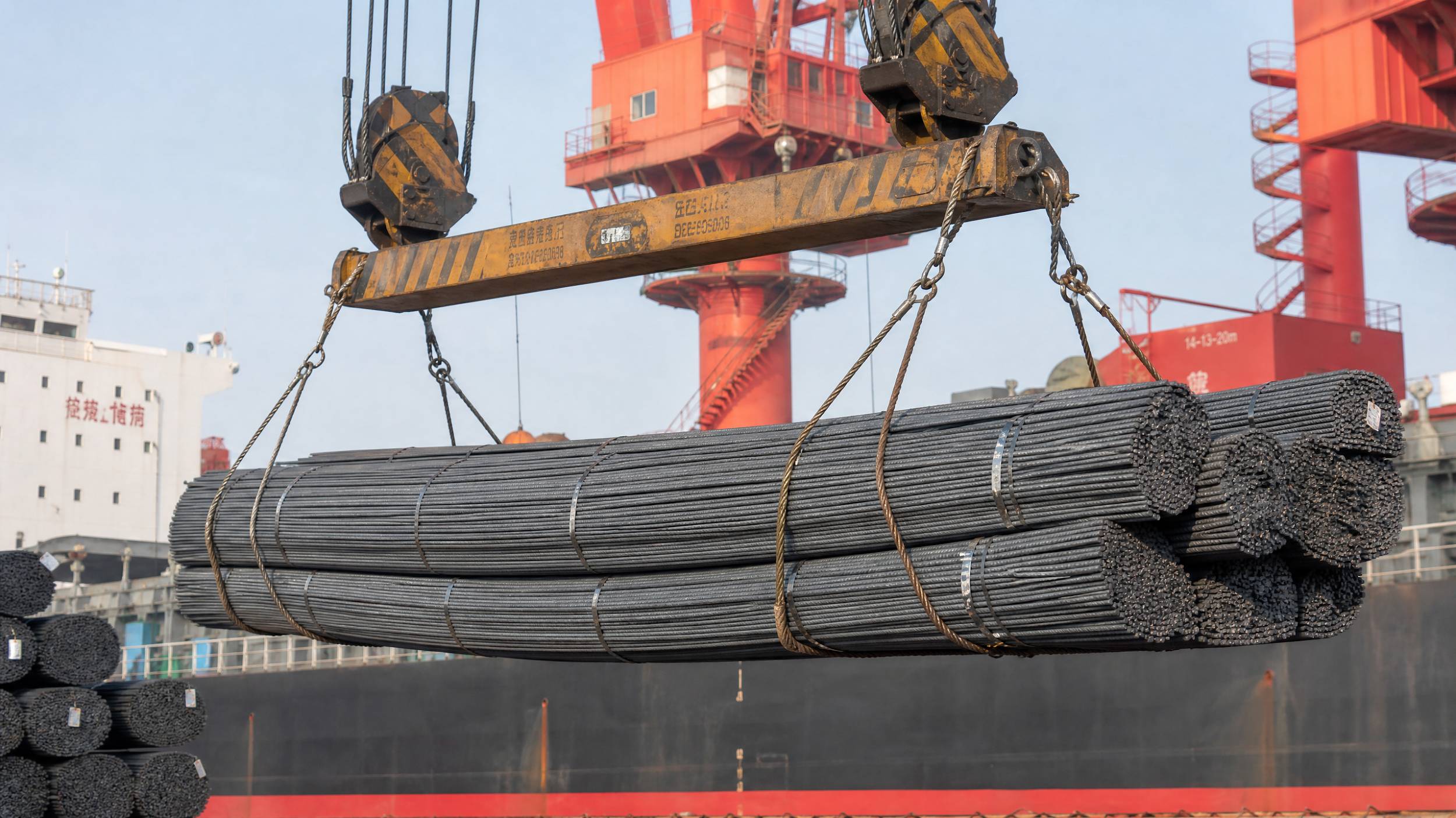 A heavy-duty crane at a Chinese port loading large bundles of structural steel rebar onto a cargo ship bound for the Philippines.