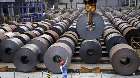 Large steel coils stored in a modern factory with worker overseeing operations