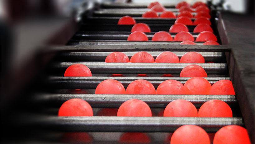Red-hot cast iron grinding balls moving on conveyor rollers during manufacturing process