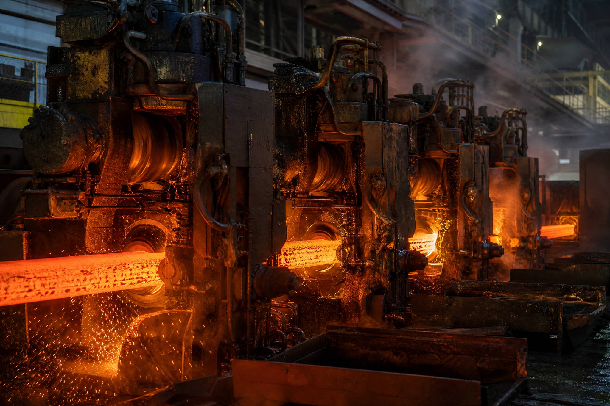 A red-hot steel rod being processed through a series of rolling stands in a modern Chinese steel mill, with sparks and intense heat visible.