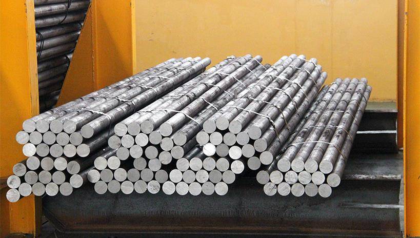 Neatly stacked bundles of steel grinding rods, secured with steel straps and featuring clear industrial labels in a warehouse.
